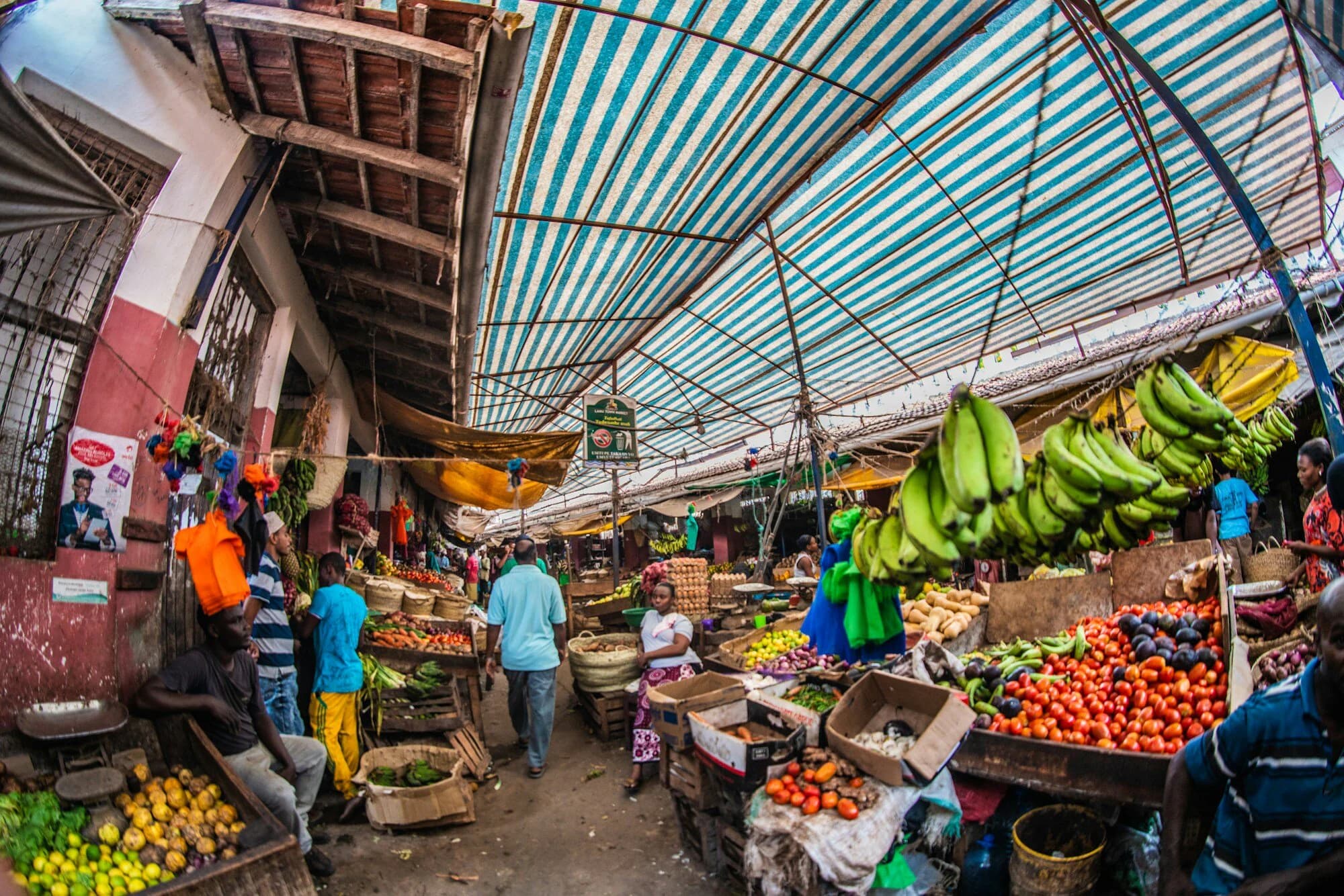 A busy covered market in Kenya with bananas, tomatoes and fruit stalls